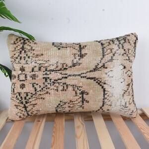 May include: A rectangular throw pillow with a beige background and a black and brown floral pattern. The pillow is sitting on a wooden slatted surface.