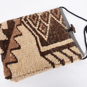 May include: A beige and brown patterned fabric bag with a black strap and a wooden toggle closure.
