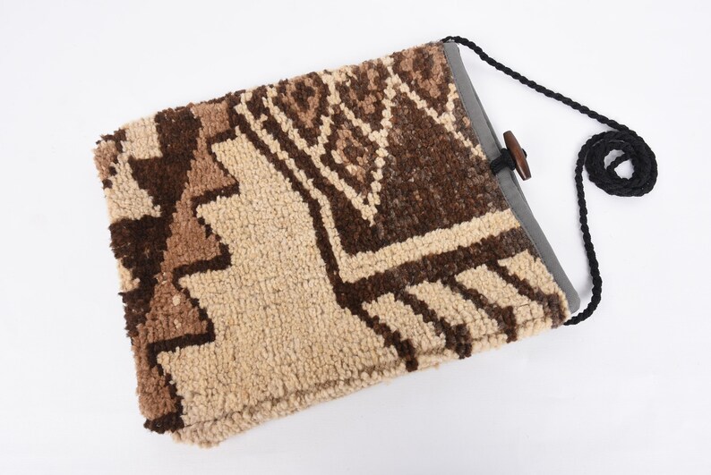 May include: A beige and brown patterned fabric bag with a black strap and a wooden toggle closure.