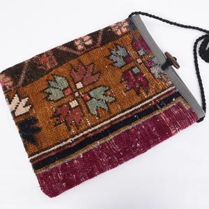May include: A brown, red, and black patterned fabric bag with a gray fabric flap and a black strap. The bag has a wooden toggle closure.