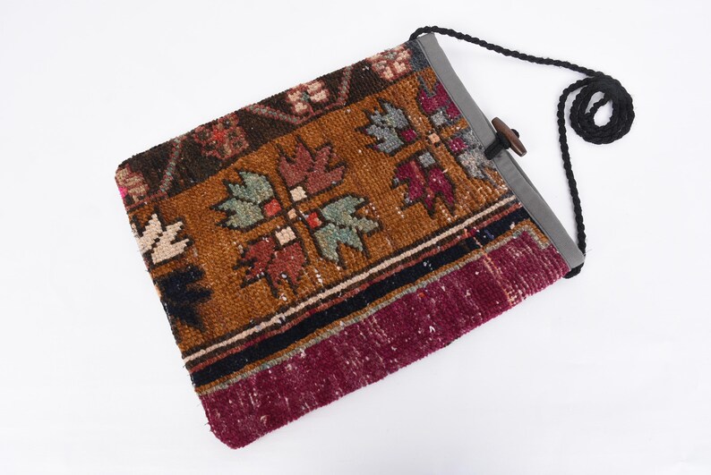 May include: A brown, red, and black patterned fabric bag with a gray fabric flap and a black strap. The bag has a wooden toggle closure.