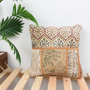 May include: A decorative throw pillow with a patchwork design featuring a variety of colors and patterns, including beige, brown, red, and white. The pillow is made from a woven fabric and has a fringed edge.