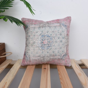 May include: A pink and blue patterned throw pillow with a floral design. The pillow is sitting on a wooden slatted surface.
