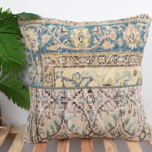 Op de afbeelding: Vierkant decoratief kussen met een patchwork ontwerp. Het kussen heeft een combinatie van blauwe, beige en lichtgroene kleuren. Het kussen heeft een vintage, distressed look, met een bloemen- en geometrisch patroon.