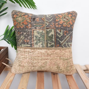 May include: A decorative pillow with a patchwork design featuring a mix of brown, green, and orange colors. The pillow is made from a vintage rug and has a frayed edge.