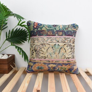 May include: A square cushion with a colourful patchwork design. The cushion is made from a variety of fabrics, including a light blue fabric with a floral pattern, a beige fabric with a geometric pattern, and a pink fabric with a striped pattern.