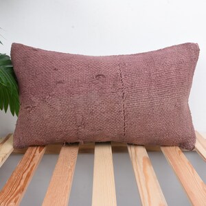 May include: A rectangular, mauve-colored pillow with a textured surface. The pillow is placed on a wooden bed frame. The pillow is a decorative item for a bed or sofa.