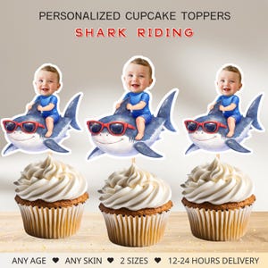 May include: Personalized cupcake toppers featuring a baby riding a shark, wearing sunglasses. The toppers are placed on cupcakes with white frosting. Text at the top reads "PERSONALIZED CUPCAKE TOPPERS SHARK RIDING".