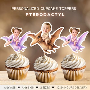 Puede incluir: Cupcakes con adornos de Pterodáctilo personalizados con la cara de un bebé. Los adornos tienen forma de Pterodáctilo con un bebé montado. Los cupcakes tienen glaseado blanco y moldes marrones. El texto de la imagen dice "PERSONALIZED CUPCAKE TOPPERS PTERODACTYL".