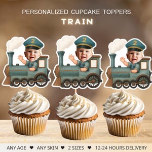 Może przedstawiać: Spersonalizowane dekoracje na babeczki z motywem pociągu, twarzą dziecka, niebieską czapką z numerem 2 i napisem "TRAIN". Ozdoby znajdują się nad babeczkami z białym lukrem. Tekst brzmi "ANY AGE", "ANY SKIN", "2 SIZES" i "12-24 HOURS DELIVERY".