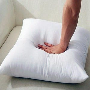 May include: A white square pillow with a hand pressing down on the center of the pillow.