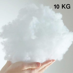 May include: A large, fluffy, white, 10 kg bag of fiberfill. The fiberfill is being held in a person's hand.