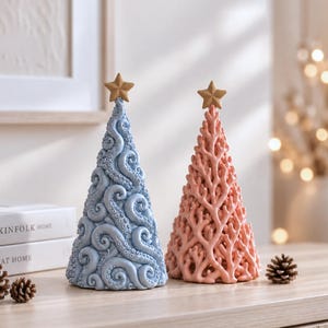 May include: Two cone-shaped decorative ornaments topped with a small star. One ornament is light blue with a textured octopus tentacle design, and the other is light pink with a branching coral-like structure. Both items stand upright.