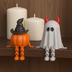 May include: Two Halloween-themed figurines sit on a shelf. One is an orange pumpkin wearing a black witch hat. The other is a white ghost with red horns. Two white candles are in the background.