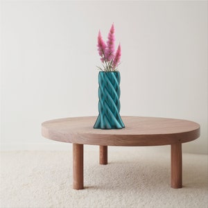 May include: A teal blue, twisted ceramic vase with a bouquet of pink flowers sits on a wooden table.