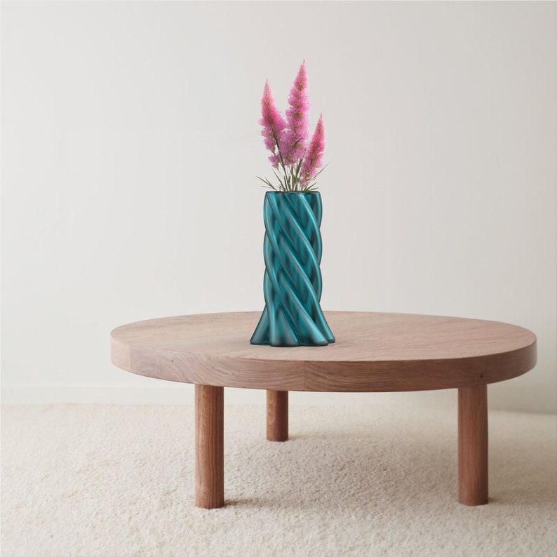 May include: A teal blue, twisted ceramic vase with a bouquet of pink flowers sits on a wooden table.