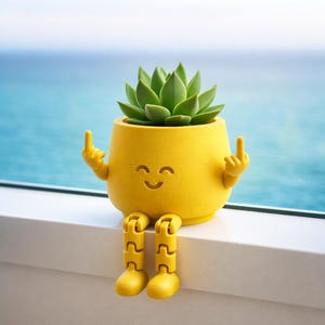 May include: A yellow ceramic planter with a smiling face, arms, and legs, holding up its middle fingers. The planter holds a green succulent plant. The planter is sitting on a white ledge with a blue ocean background.