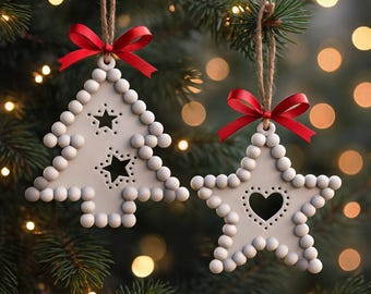Puede incluir: Dos adornos navideños blancos cuelgan de una cuerda, un árbol y una estrella, cada uno con un lazo rojo. El árbol tiene recortes de estrellas y la estrella tiene un recorte de corazón. Ambos están decorados con pequeñas cuentas redondas.