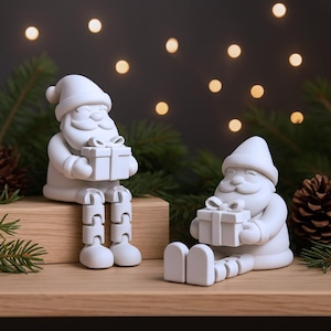 May include: Two white Santa Claus figurines, one seated with articulated legs and the other reclining. Each holds a gift box. The background features blurred lights and evergreen branches, creating a festive holiday scene.