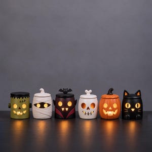 Pu&ograve; includere: Sei portacandele in ceramica a tema Halloween a forma di mostro verde, mummia bianca, vampiro scuro con ali di pipistrello, teschio bianco, zucca arancione e gatto nero, ciascuno illuminato dall'interno con una luce calda e accogliente.