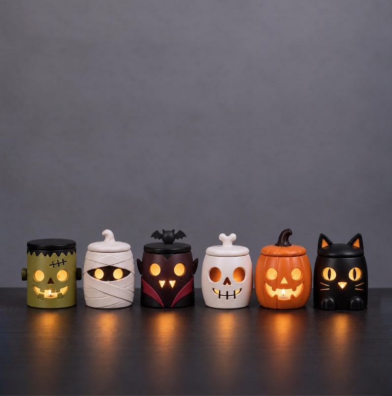 Pu&ograve; includere: Sei portacandele in ceramica a tema Halloween a forma di mostro verde, mummia bianca, vampiro scuro con ali di pipistrello, teschio bianco, zucca arancione e gatto nero, ciascuno illuminato dall'interno con una luce calda e accogliente.