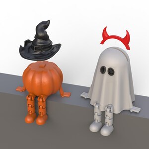 May include: Two Halloween-themed figurines: an orange pumpkin with a black witch hat and a white ghost with red devil horns. Both have articulated legs and arms, sitting on a gray surface against a white background.
