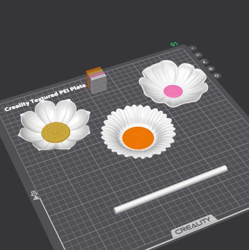 Op de afbeelding: Een digitale interface toont een Creality Textured PEI-plaat met drie witte bloemvormige schalen met gele, oranje en roze centra, samen met een witte cilindrische staaf en een klein veelkleurig kubusblok op een rasterindeling.