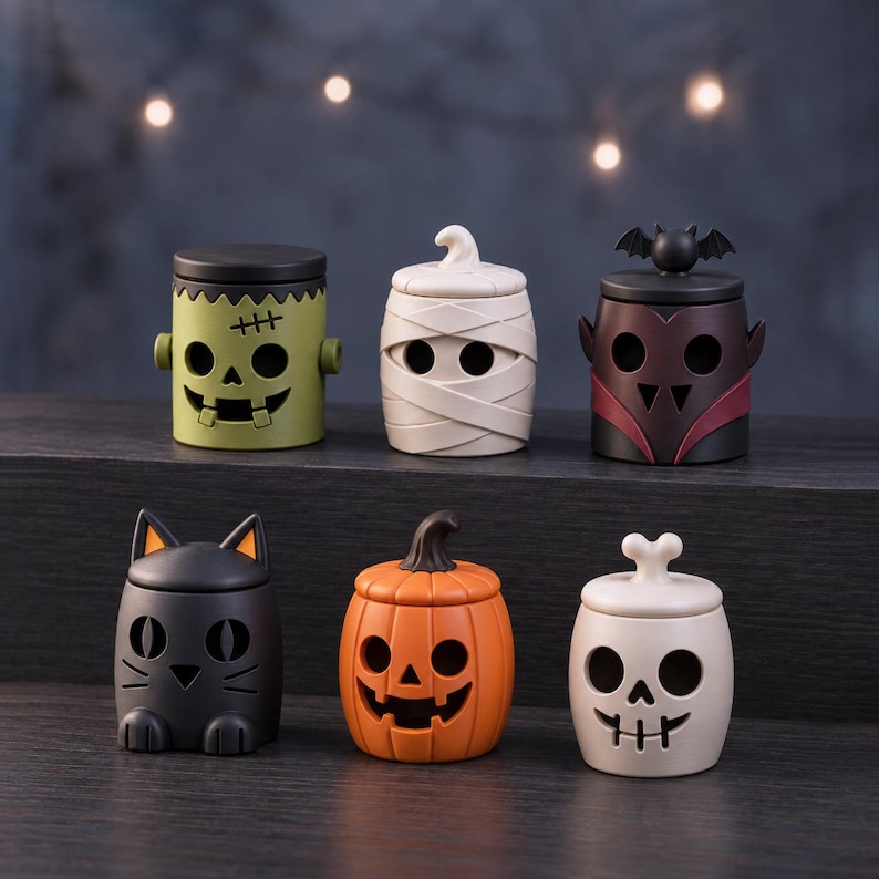Pu&ograve; includere: Un set di sei piccoli contenitori decorativi a tema Halloween: un mostro di Frankenstein verde, una mummia beige, un vampiro nero con pipistrello, un gatto nero, una zucca arancione e un teschio beige con un osso come manico.