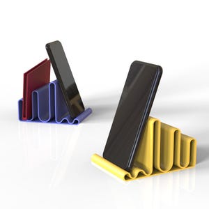 Puede incluir: Dos soportes para teléfono, uno azul y otro amarillo, con un diseño ondulado. Cada soporte sostiene un teléfono inteligente negro en posición vertical.