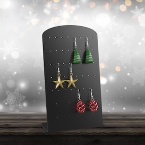 May include: Black earring display stand with a variety of earrings, including green Christmas trees, gold stars, and red baubles.