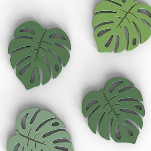 Puede incluir: Cuatro posavasos verdes con forma de hoja de Monstera. Cada posavasos tiene un dise&ntilde;o detallado de hoja con secciones recortadas. Los posavasos son de color verde liso y est&aacute;n dispuestos sobre un fondo blanco.