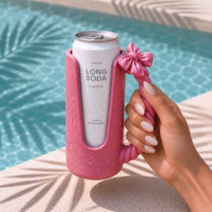 May include: A pink can holder with a textured surface and a twisted handle topped with a bow. The holder contains a 330 ml silver can labeled LONG SODA CLASSIC CRISP & REFRESHING. The holder is covered in water droplets and has a vertical cutout design.