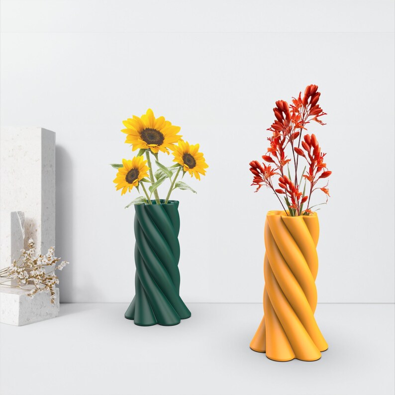 May include: Two ceramic vases with a twisted design. One vase is green and holds a bouquet of yellow sunflowers. The other vase is yellow and holds a bouquet of red flowers.