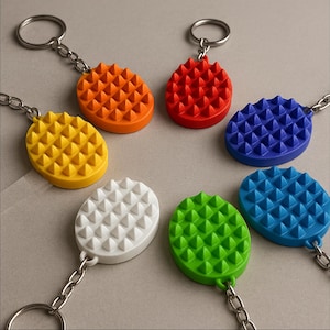 May include: A collection of colorful keychains in various shades, including orange, red, blue, yellow, white, green, and teal. Each keychain features an oval-shaped design with a textured, spiky surface and a silver chain and ring.