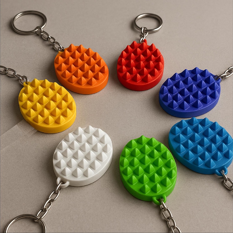 May include: A collection of colorful keychains in various shades, including orange, red, blue, yellow, white, green, and teal. Each keychain features an oval-shaped design with a textured, spiky surface and a silver chain and ring.