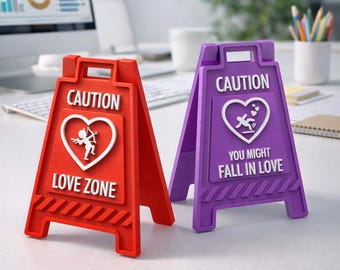 Puede incluir: Dos señales de precaución coloridas, una roja y otra morada, con texto y gráficos blancos. La señal roja dice "CAUTION LOVE ZONE" con un corazón y un gráfico de cupido. La señal morada dice "CAUTION YOU MIGHT FALL IN LOVE".
