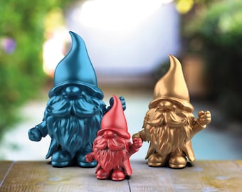 Può includere: Tre gnomi da giardino, uno blu, uno dorato e uno rosso, in piedi su una superficie di legno. Gli gnomi indossano tutti cappelli e hanno barbe bianche.