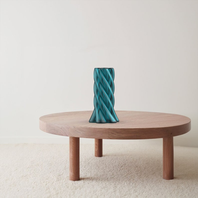 May include: A teal blue glass vase with a twisted design sits on a wooden table with three legs.
