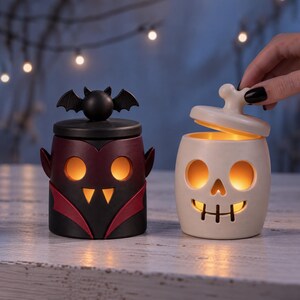 Pu&ograve; includere: Due portacandele in ceramica a forma di personaggi di Halloween. Uno &egrave; un vampiro nero e rosso con un coperchio a forma di pipistrello. L'altro &egrave; un teschio color crema con un manico a forma di osso. Entrambi emettono una calda luce arancione.
