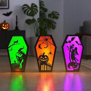 May include: Three coffin-shaped Halloween decorations with illuminated interiors. The first glows green with a witch silhouette, the second orange with a pumpkin and spider, and the third purple with a dancing couple. A festive home decor item.