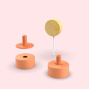 Pode incluir: Duas bases cil&iacute;ndricas laranja com pinos centrais, uma tampa circular laranja com um pino central e uma esponja circular amarela presa a uma haste branca fina. Os objetos est&atilde;o dispostos sobre um fundo rosa claro s&oacute;lido.