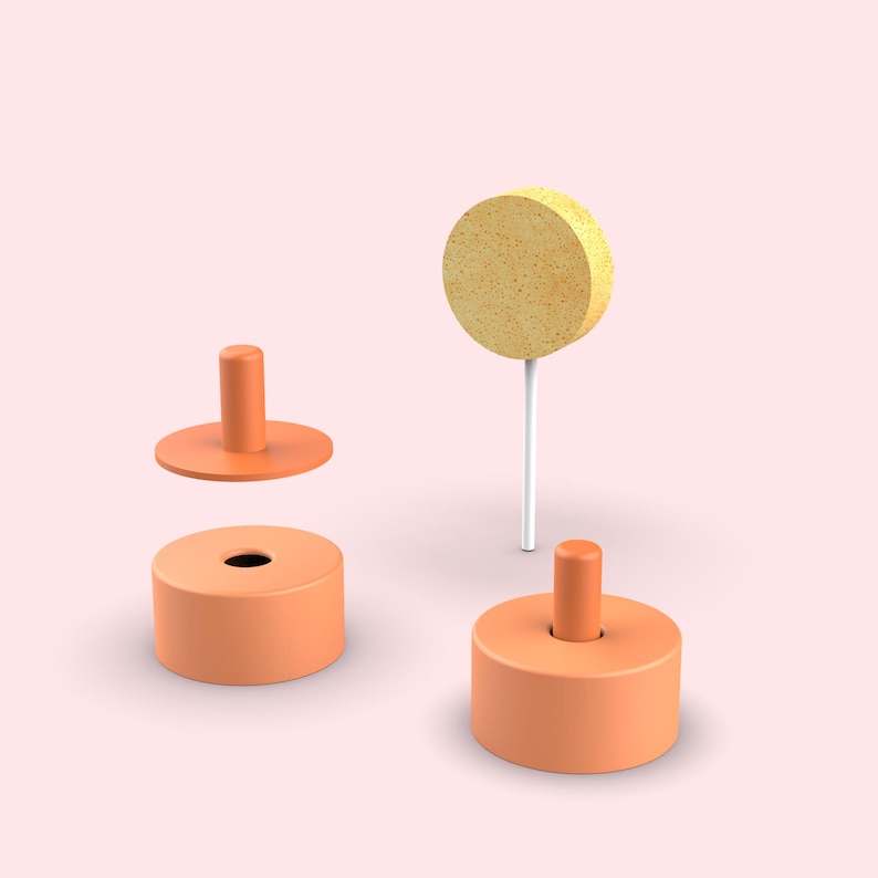 Pode incluir: Duas bases cil&iacute;ndricas laranja com pinos centrais, uma tampa circular laranja com um pino central e uma esponja circular amarela presa a uma haste branca fina. Os objetos est&atilde;o dispostos sobre um fundo rosa claro s&oacute;lido.