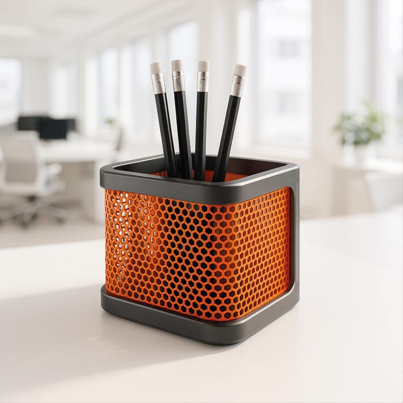 May include: A modern desk organizer with a black frame and orange honeycomb mesh sides. The organizer holds five black pencils with white erasers. The office supply container sits on a white surface.
