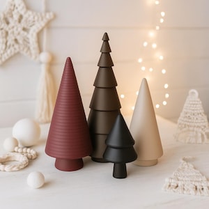 May include: A collection of four decorative wooden Christmas trees in varying shades of red, brown, and beige. The trees are arranged on a white surface, with a star-shaped decoration and string lights in the background. The trees range in height.