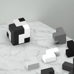Puede incluir: Un conjunto de formas geom&eacute;tricas de madera en negro, blanco y gris. Las formas est&aacute;n dispuestas sobre una superficie de m&aacute;rmol blanco.