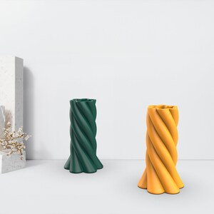 May include: Two decorative twisted candles, one green and one yellow, on a white surface.