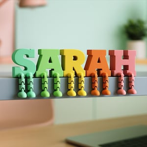 May include: A colorful, whimsical desk accessory spelling out the name "SARAH". Each letter is a different color: green, yellow, orange, and pink. The letters have attached legs, adding a playful touch to the design.