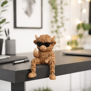 May include: A brown Highland cow figurine wearing black sunglasses and giving the middle finger. The figurine has articulated legs and is sitting on a dark surface. The cow has a shaggy coat and small horns.