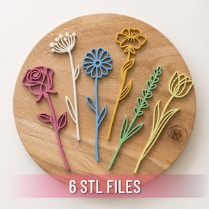 May include: A wooden cutting board displays six colorful, laser-cut flower designs. The flowers include a pink rose, white sprig, blue daisy, yellow flower, green lavender, and yellow tulip. The text "6 STL FILES" is at the bottom.