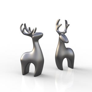 May include: Two metallic silver deer figurines. The deer have stylized bodies with arched legs and large antlers. The figurines are smooth and reflective, with a modern, minimalist design. They are set against a white background.